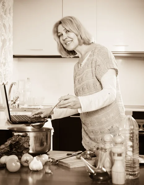 Huisvrouw met behulp van de laptop tijdens het koken — Stockfoto