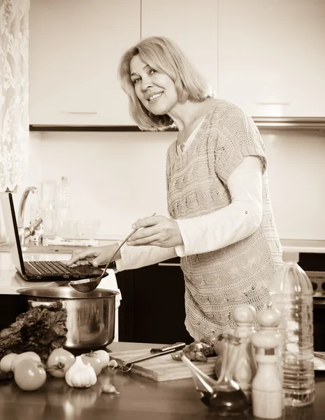 Dona de casa usando laptop enquanto cozinha — Fotografia de Stock