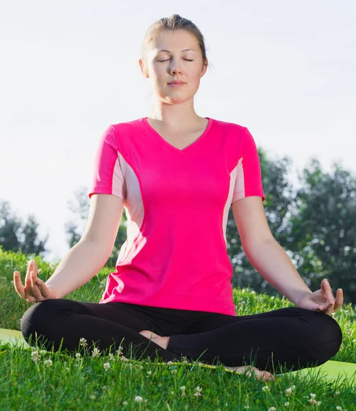 Pembe tişörtlü atletik kadın oturmuş meditasyon yapıyor. — Stok fotoğraf