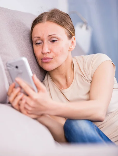 Femme inquiète sur le canapé avec téléphone — Photo