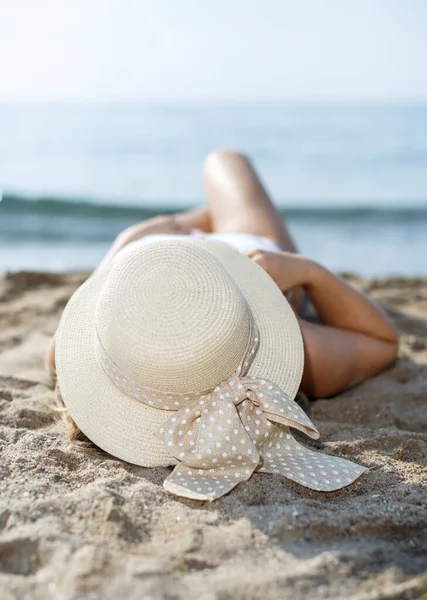 Szoros kép a lány fürdőruhában és kalapban vesz napfürdőt a homokos strandon — Stock Fotó