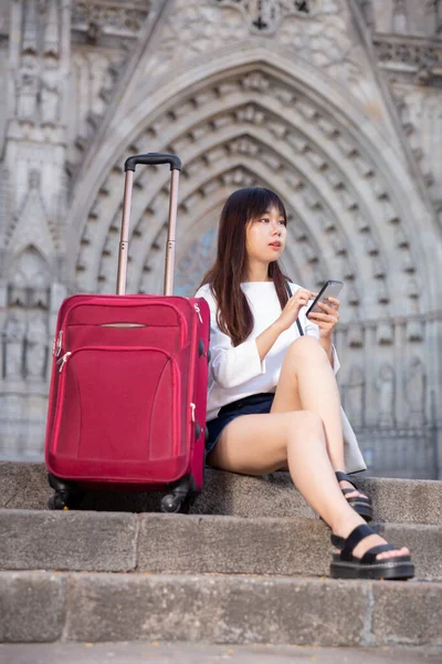 Young chinese woman tourist sits on a stone staircase and writes sms by phone — Stock Photo, Image