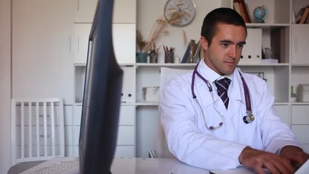 Medico in maschera medica protettiva seduto sul posto di lavoro con il computer nel suo ufficio — Video Stock
