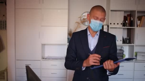 Portret van een positieve zakenman in beschermend masker met map van documenten op kantoor — Stockvideo