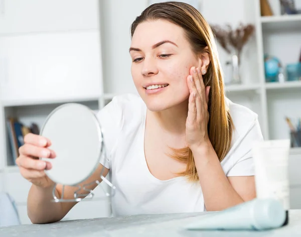 Leende hona tittar på sin hud i spegeln — Stockfoto