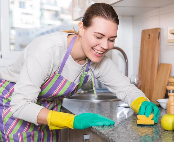 Jonge huisvrouw in handschoenen is schoonmaken keuken met wasmiddel — Stockfoto