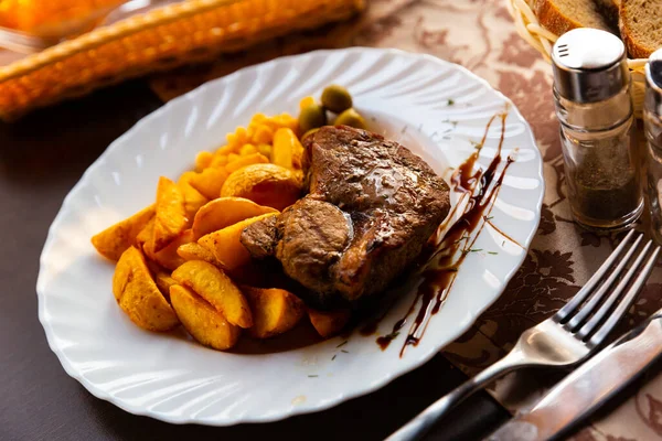 Appetizing steak in honey marinade with side dish of potatoes and olives — Stock Photo, Image