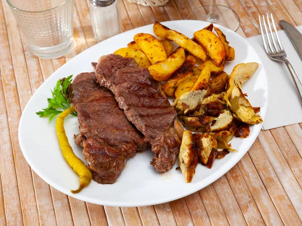 Delicious beef steak with baked potatoes and artichokes — Stock Photo, Image