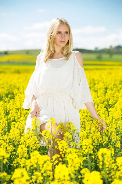 Mujer joven posando en campo de colza de semillas oleaginosas amarillas vestida de blanco —  Fotos de Stock