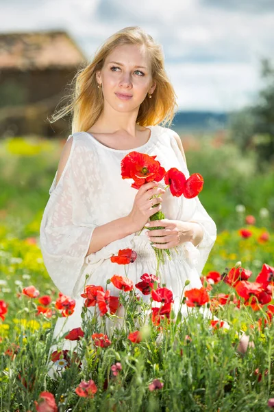 Beautiful young female in white dress holding bouquet of poppy flowers — Stock Photo, Image