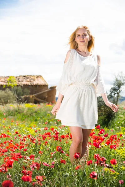 Frau im weißen Kleid spaziert durch ein Mohnfeld und genießt — Stockfoto