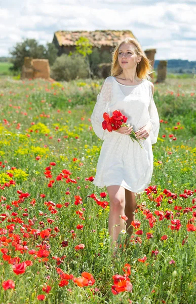 Frau in weißem Kleid geht und hält Strauß Mohnpflanzen in der Hand — Stockfoto