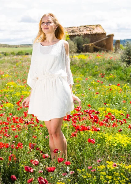 Weibchen im weißen Kleid spazieren durch ein Mohnfeld mit wilden Blumen — Stockfoto