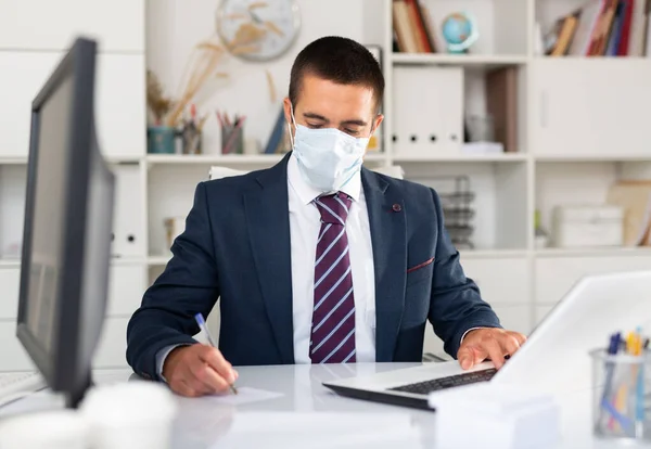 Homem de negócios focado em máscara facial trabalhando no escritório — Fotografia de Stock