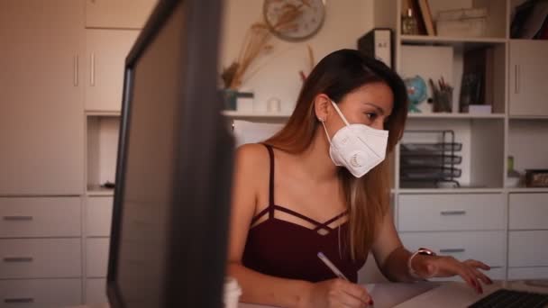 Θετική λατίνα γυναίκα με προστατευτική μάσκα και casual ντύσιμο που εργάζεται μόνη της με laptop και χαρτιά στο γραφείο Royalty Free Βίντεο Αρχείου