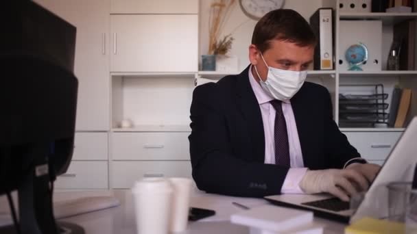 Zakenman in beschermend masker werkt alleen met laptop en papieren op kantoor — Stockvideo