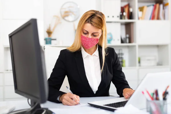 Affärskvinna i färgad medicinsk mask arbetar med bärbar dator — Stockfoto