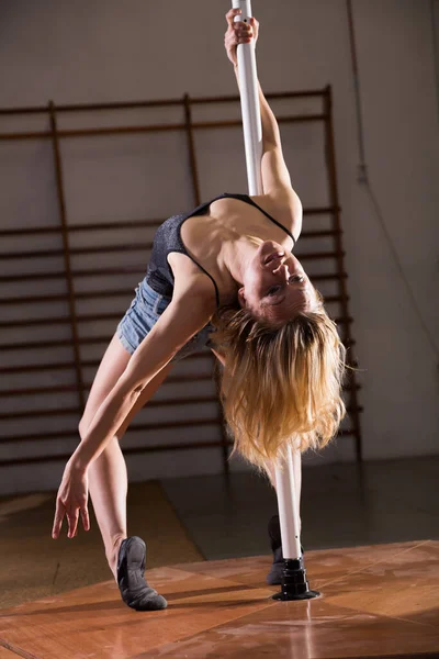 Mujer joven en pantalones cortos de mezclilla practicando pole dancing —  Fotos de Stock