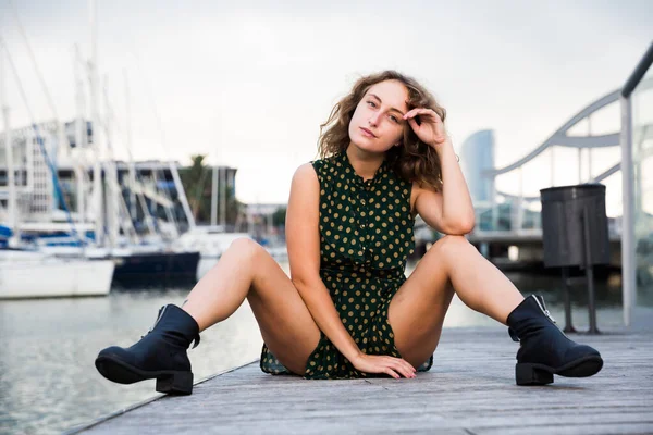 Chica sexy en vestido sentado en el muelle con barcos en el fondo en Barcelona — Foto de Stock