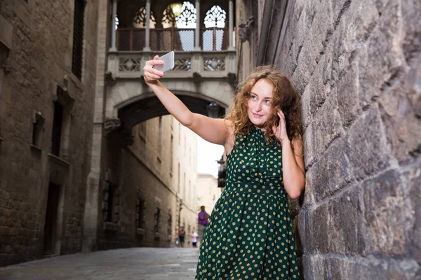 Jovencita alegre de pie cerca de la pared de ladrillo y hacer selfie con el teléfono — Foto de Stock