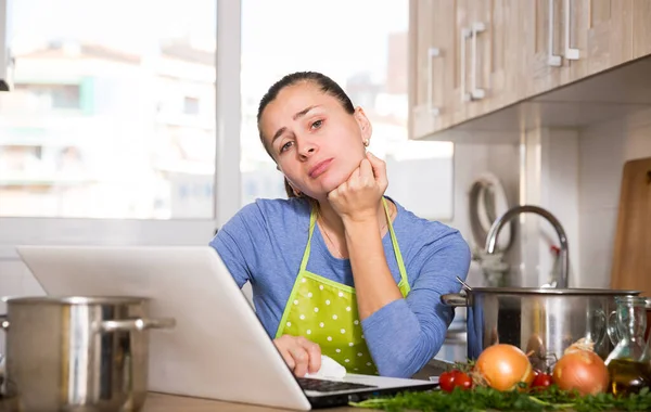 Laptop ekranında yemek tarifi okuyan üzgün genç bir kadın. — Stok fotoğraf
