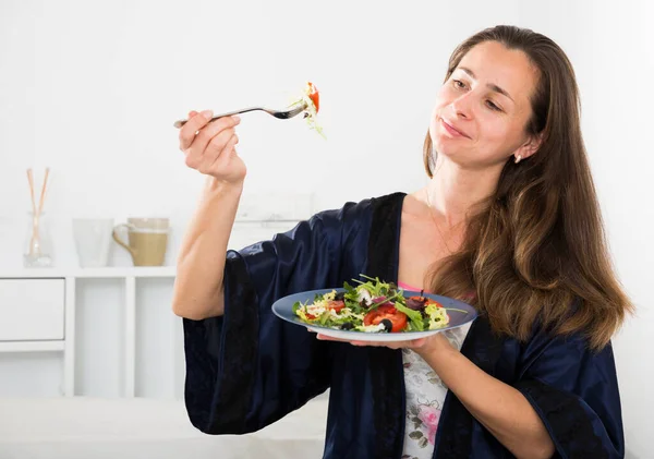 Kvinna i blå sidenrock äter sallad i sängen — Stockfoto