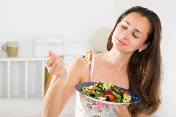 Положительная красивая женщина держит вилку и ест овощной салат в постели — стоковое фото