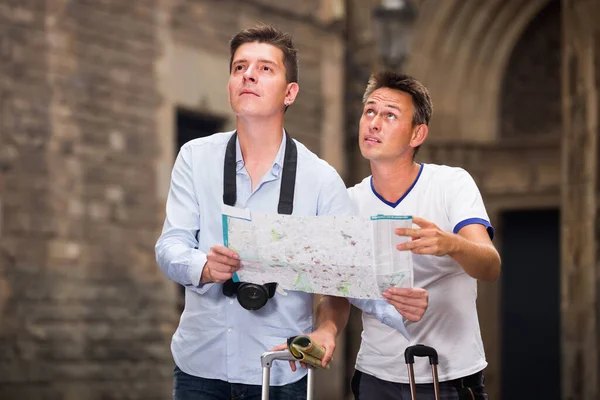 Hombres positivos sosteniendo el mapa en las manos y buscando su camino —  Fotos de Stock