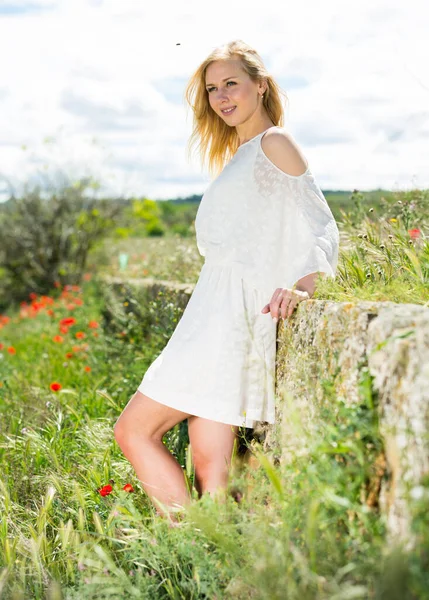 Frau in weißem Kleid posiert in der Nähe von Feldern mit wilden Blumen — Stockfoto