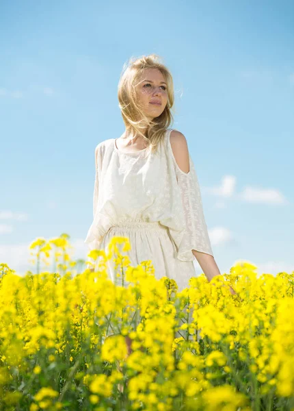 Jeune femme dans un champ de colza jaune posant en robe blanche — Photo