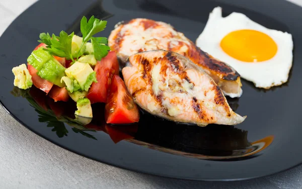 Fried salmon on black plate with fried egg, tomatoes, avocado — Stock Photo, Image