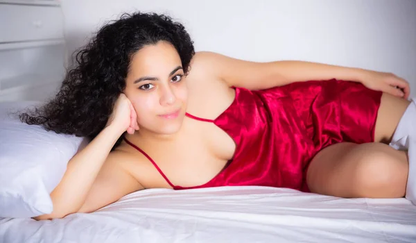 빨간 란제리를 입은 갈색 머리 여자가 침대에서 즐겁게 누워 있는 모습 — 스톡 사진