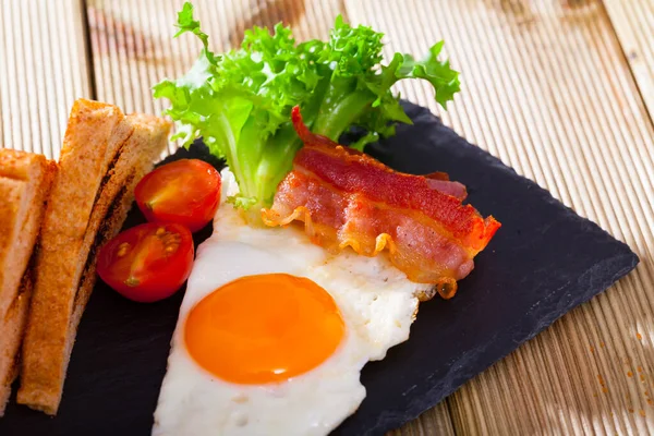 Huevos cocidos con tocino, pan tostado, tomates y lechuga en plato sobre mesa —  Fotos de Stock