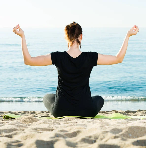 Mujer con camiseta negra está sentada de espaldas y practicando meditación —  Fotos de Stock