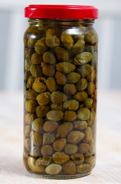 Gekneusde kappertjes in een glazen pot op houten tafel — Stockfoto