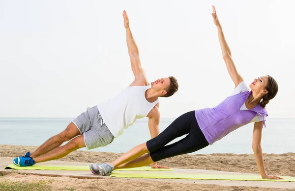 Casal exercitando poses de ioga em pé na praia — Fotografia de Stock