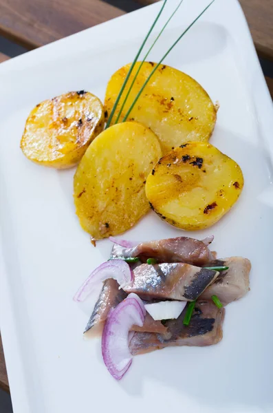 Kızarmış patates, hafif kavrulmuş ringa balığı ve soğan tabakta servis edilir. — Stok fotoğraf