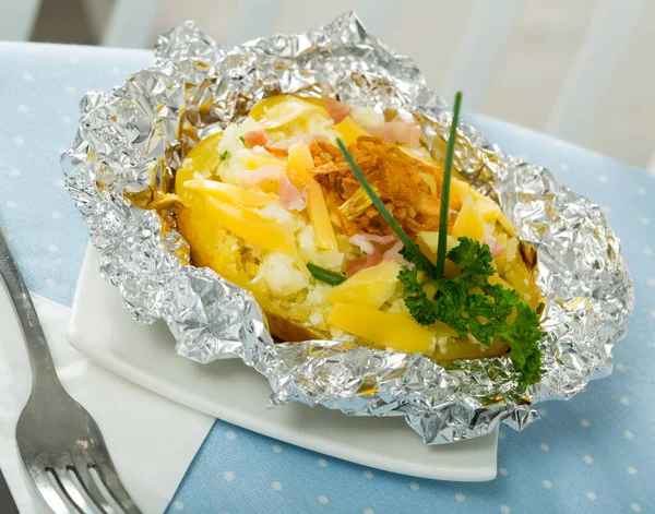 Cooked baked potatoes in foil with filling of bacon, fried onion and cheese — Stock Photo, Image