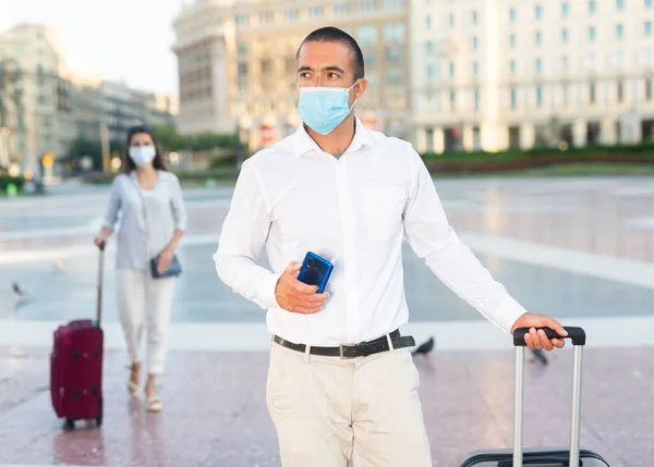 Jovem em máscara médica andando pela cidade com mala — Fotografia de Stock