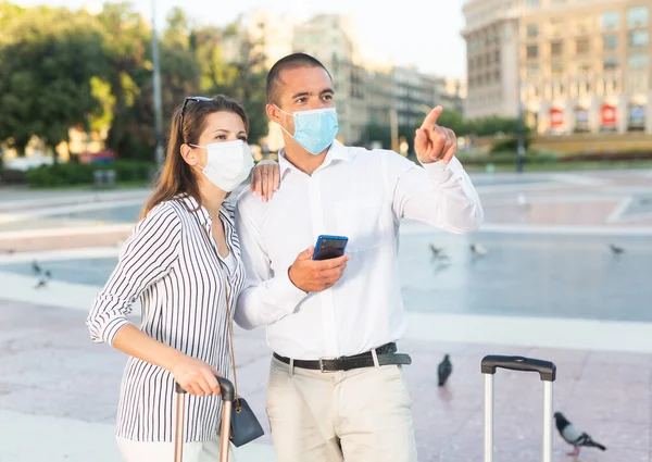 Casal de viajantes em máscaras médicas apontando para pontos turísticos em cidade estrangeira — Fotografia de Stock