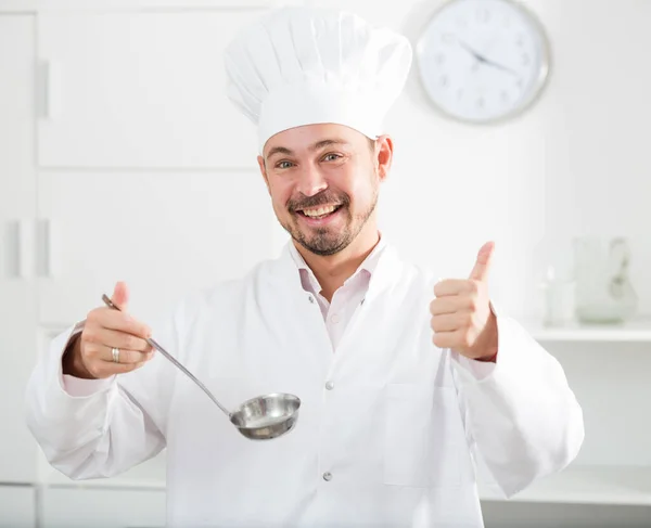 Positive young cook holding soup ladle — Stock Photo, Image