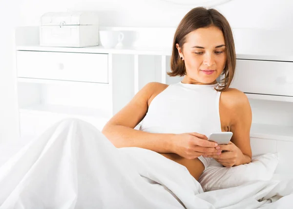 Женщина с телефоном в постели — стоковое фото