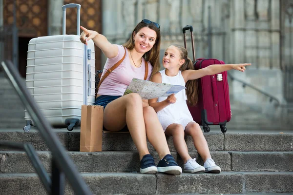 Attractive young woman with daughter resting on stairs reading paper map during vacation — Stock Photo, Image