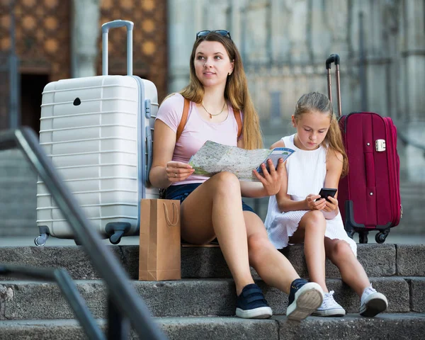 Mamma med liten flicka med hjälp av papperskarta och telefon — Stockfoto