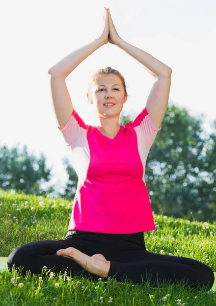 Dospělá žena v růžovém tričku sedí a cvičí meditaci — Stock fotografie