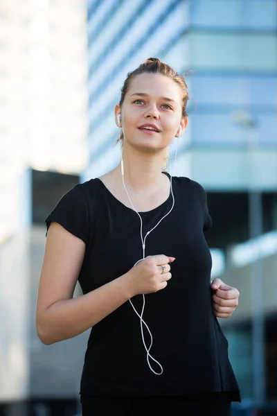 Ragazza che corre lungo le strade con le cuffie nelle orecchie — Foto Stock