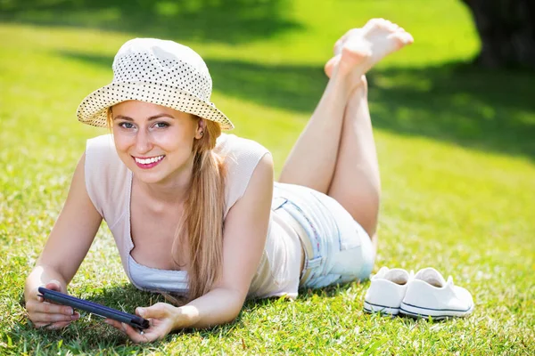 Woman lying on green grass in park and holding mobile phone in hands — Stock Photo, Image