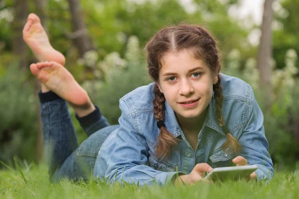 Fiatal lány használ digitális tabletta, miközben feküdt a zöld tavaszi kertben — Stock Fotó