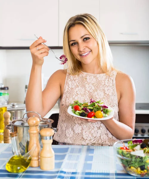 Девушка, стоящая за кухонным столом с тарелкой салата — стоковое фото