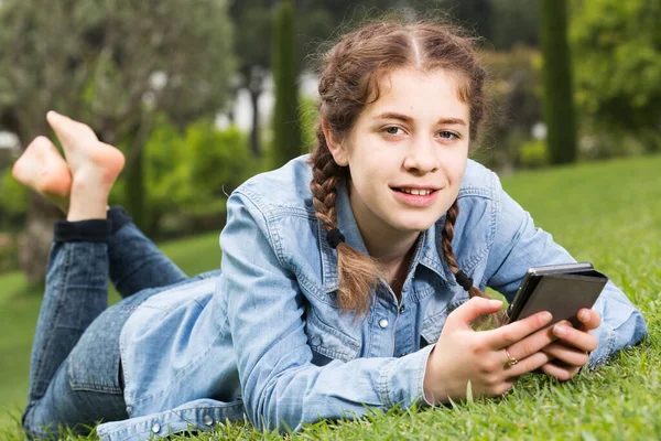 Young girl using digital tablet while lying in green spring garden — Stock Photo, Image